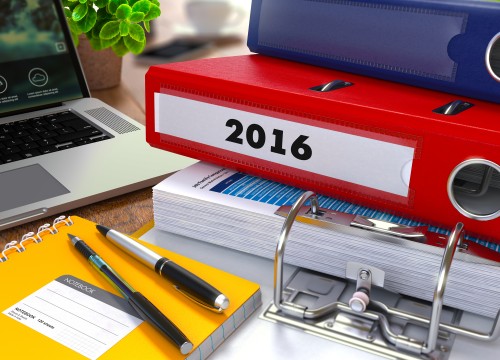 Red Ring Binder with Inscription 2016 on Background of Working Table with Office Supplies, Laptop, Reports. Toned Illustration. Business Concept on Blurred Background.