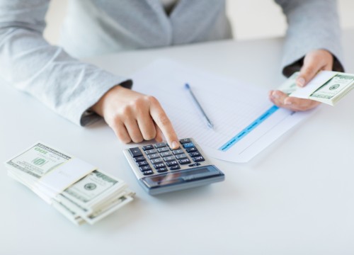 business, finance, tax and people concept - close up of woman hands counting us dollar money with calculator